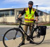 Gary Ribis, wearing a bike helmet and safety vest, poses on campus with his bicycle