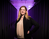 CEHC Vice Dean Jen Goodall stands between computing systems with purple lighting.
