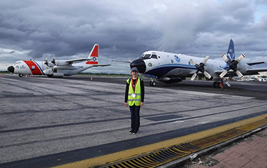 Emily Paltz stands in front of the of a United States Coast Guard plane and Kermit – the NOAA42 P-3 Hurricane Hunter.