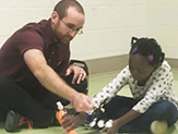 A UAlbany master's student works one on one with a child on an Arbor Hill Albany classroom floor. 