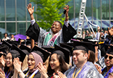 A gowned female student rises 3 feet above hundreds of other students with her arms raised.