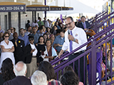 President Rodríguez, from a stairway beneath the bleachers of Casey Stadium, holds a microphone and adresses hundreds of listeners