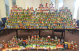 A double-section-longed table piled 3 feet high with multi-colored cans of food.