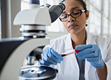 A female scientist of color examines test tube contents by a microscope