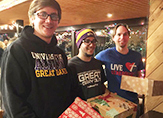 Three students pack gifts for residents of a homeless shelter.