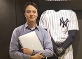 Photo of Liam Smith, junior, standing by New York Yankees uniform at MLB's Office of the Comissioner. 