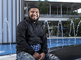 Moises Urena, a peer leader at UAlbany, sits and smiles by the side of the Main Fountain.