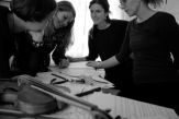 Four female members of Nordic Affect stand about a drawing table, looking at sheet music and a violin