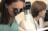 A female student research looks in a microscope as a male looks off in a lab