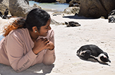 Rajanie Bhudeo lies on a beach in South Africa next to a prone penguin. 
