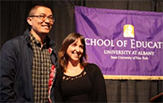 A student research and prof stand before a School of Education banner