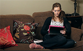 A young woman student works on laptop computer from her couch