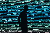 a silhoetted man stands with thousands of blue circuitries going off behind him