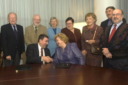 Deans and officials look on as Interim President Philip and Rector Shaidenko shake hands on the agreement. 