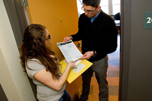 A UAlbany student hands out a census form to another UAlbany student in a door way.