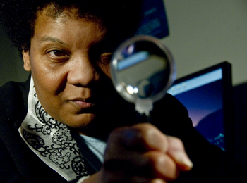 UAlbany criminologist Frankie Bailey peers through a magnifying glass.