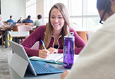 Two students look over a laptop at a table in the University Science Library