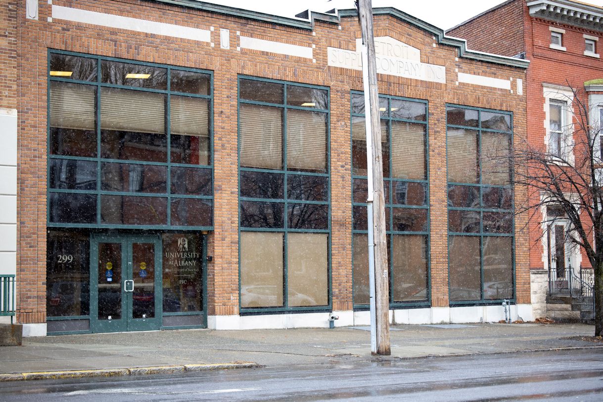 A brick-front building with large windows stands on a city street with snow falling