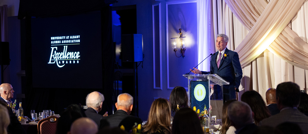 An award recipient stands at a podium inside a ballroom.
