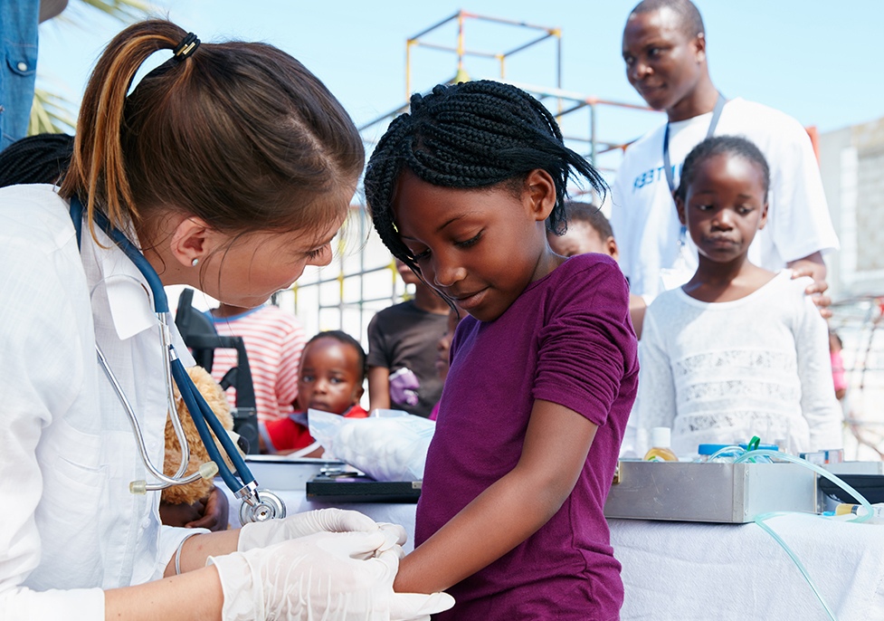 Woman in a lab coat with a stethascope working on the arm of a child