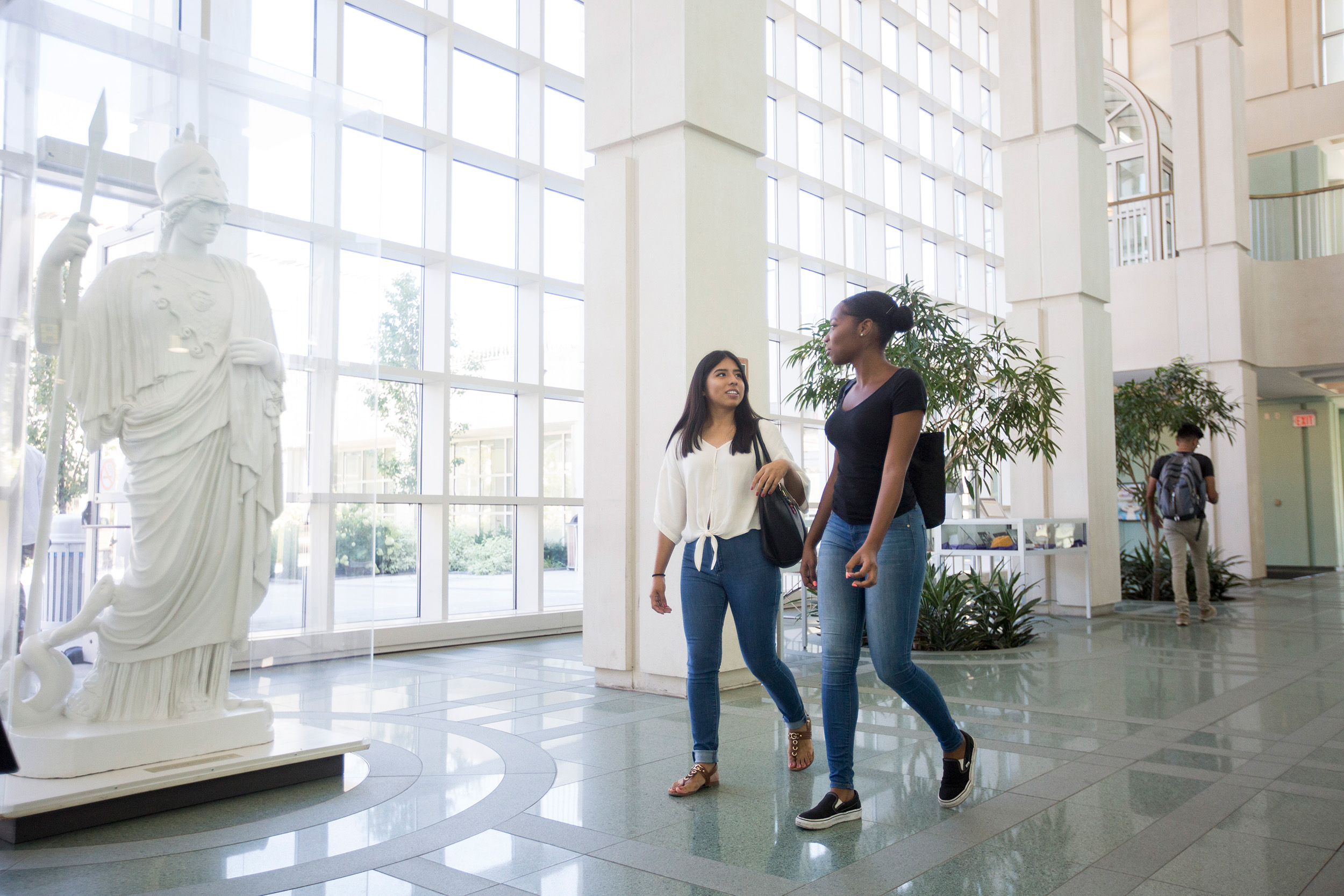 Two students walk past the statue of Minerva, talking to each other.