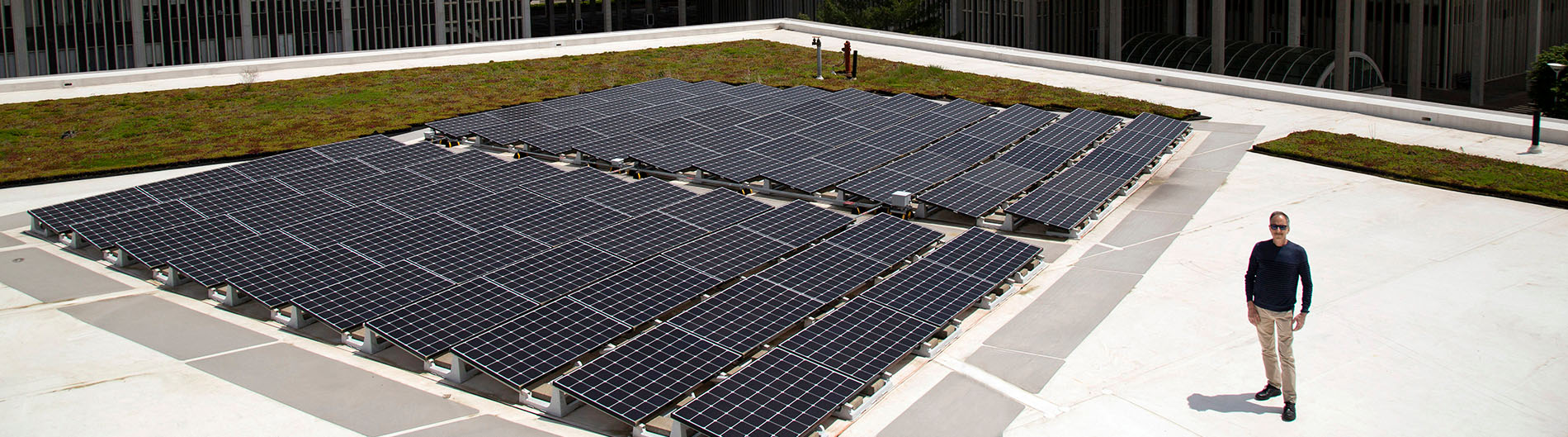 Richard Perez of ASRC, and solar panels on the roof of a UAlbany building with tower in the background.