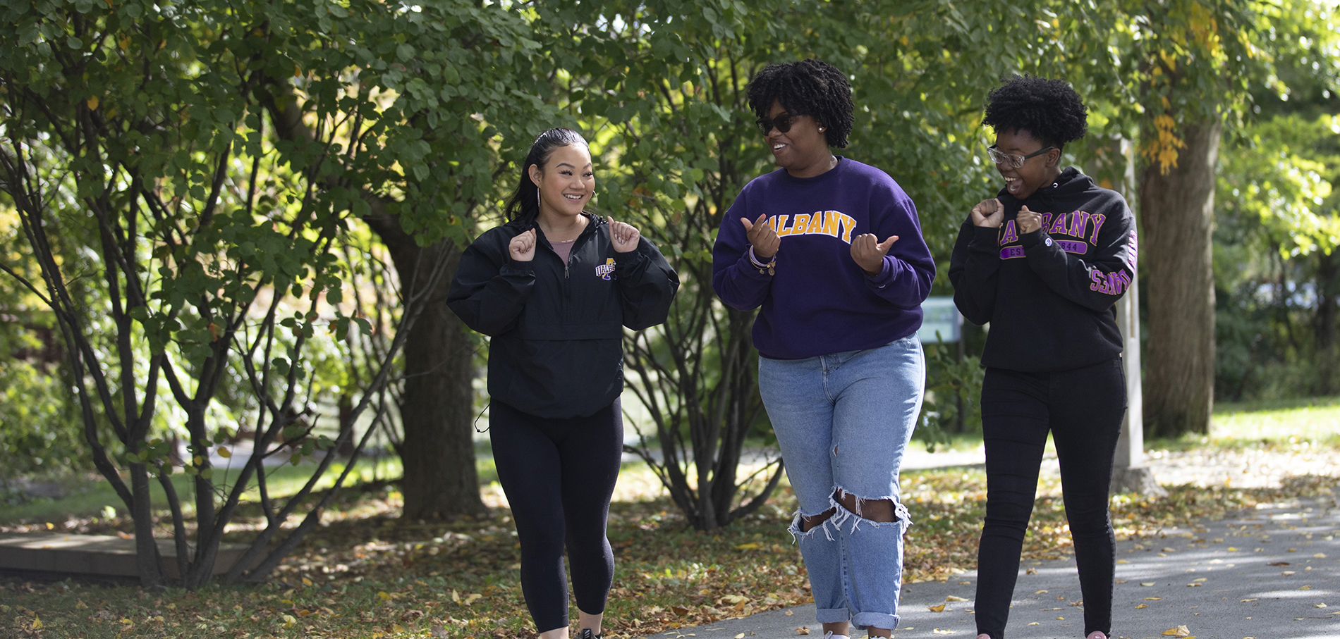 Three female UAlbany students walking and smiling on campus.