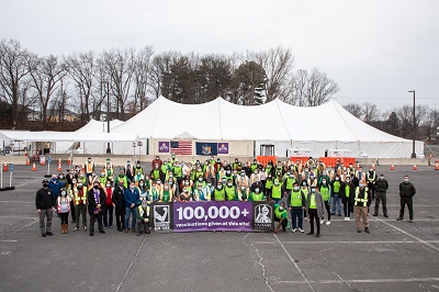 Volunteers hold up a sign to celebrate the 100,000th vaccine administered at the New York State COVID-19 vaccination site on campus.