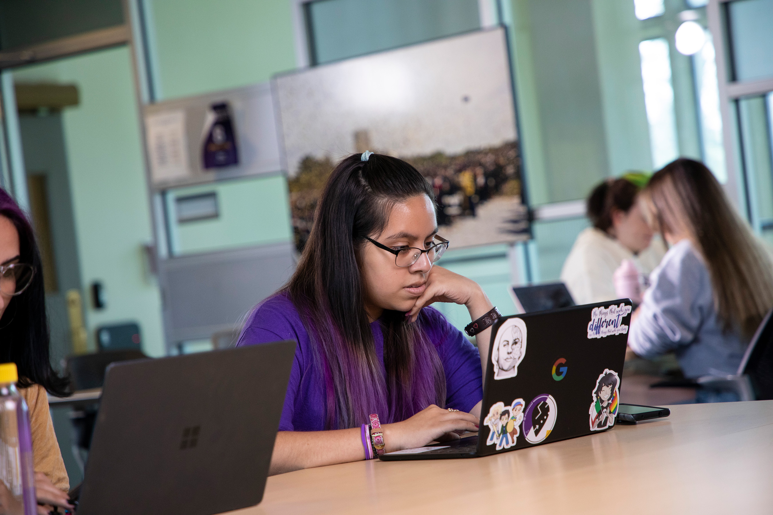 A student sits at a desk using their laptop in a classroom.