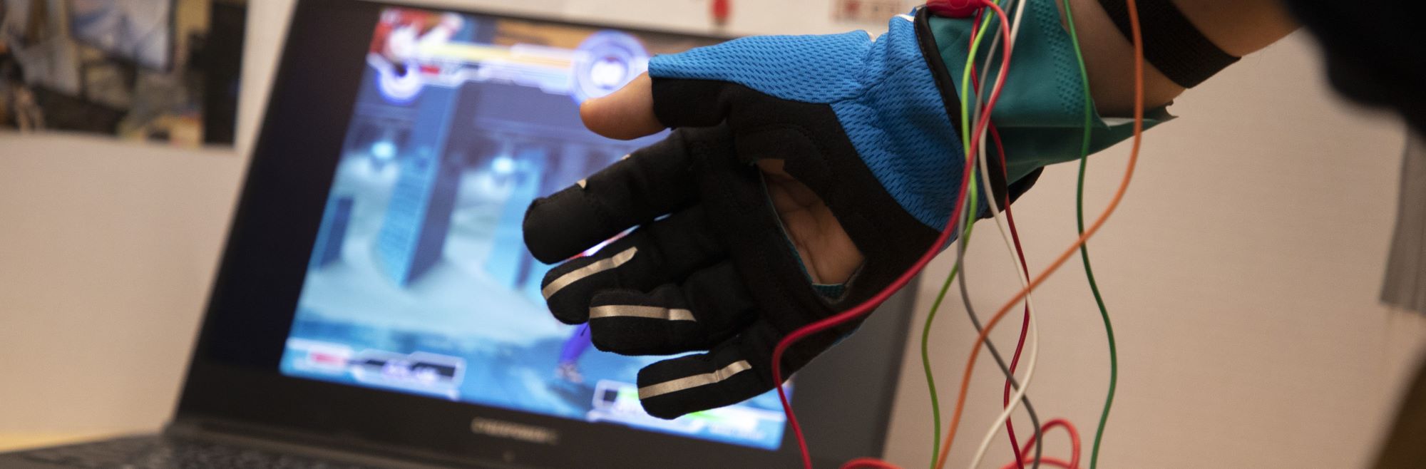Student wearing a controller glove wired up to a laptop.