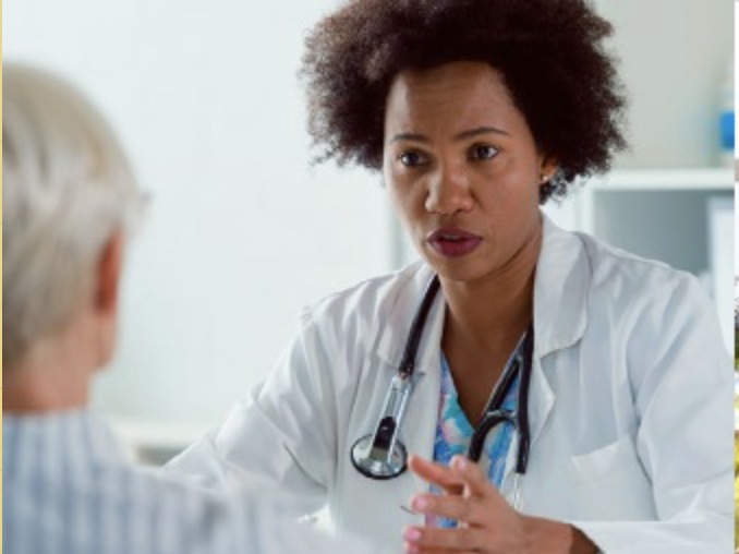A doctor wearing a white coat speaks to a patient.