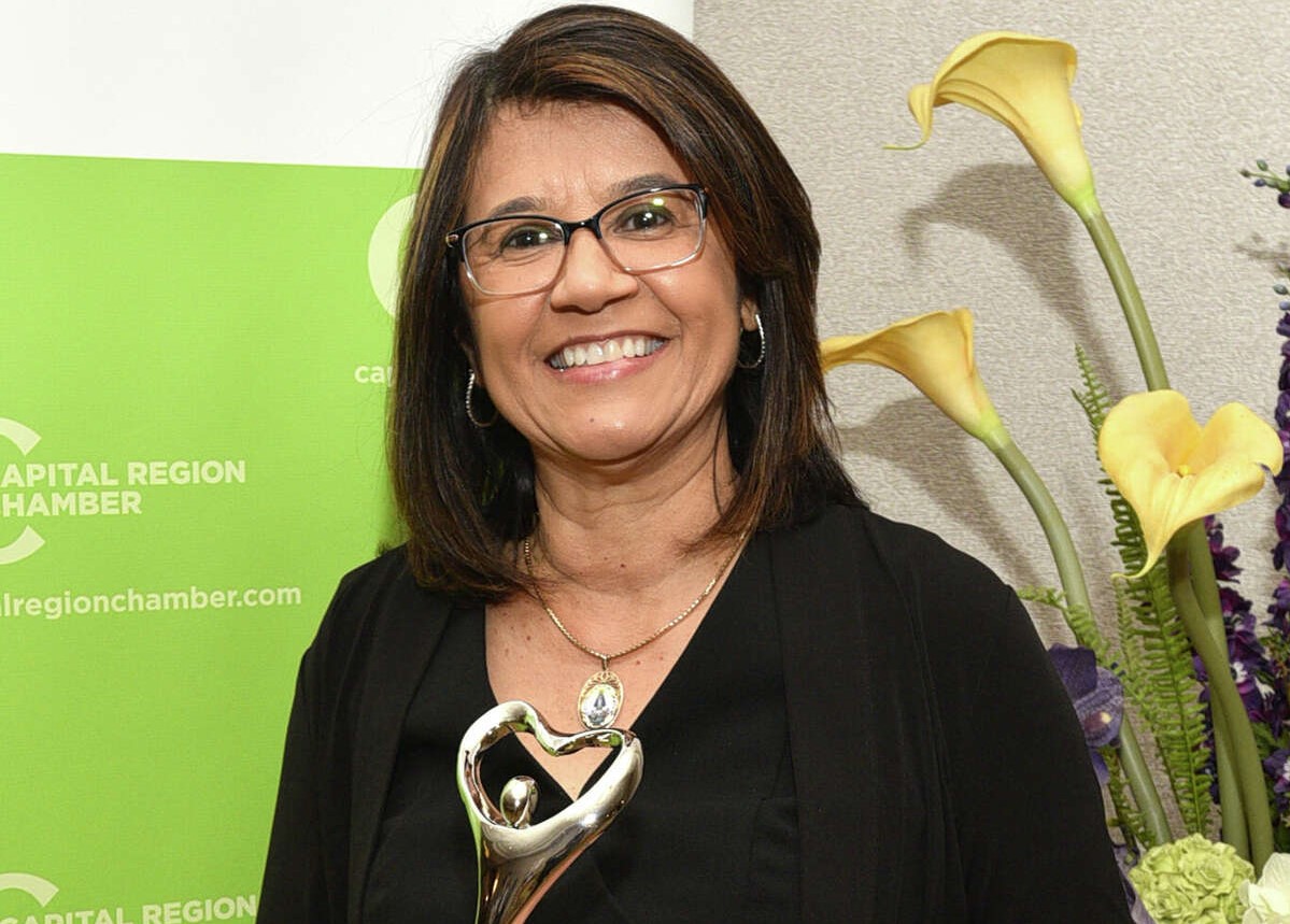 Dr. Gladys Cruz smiling wearing glasses and black dress, holding an award