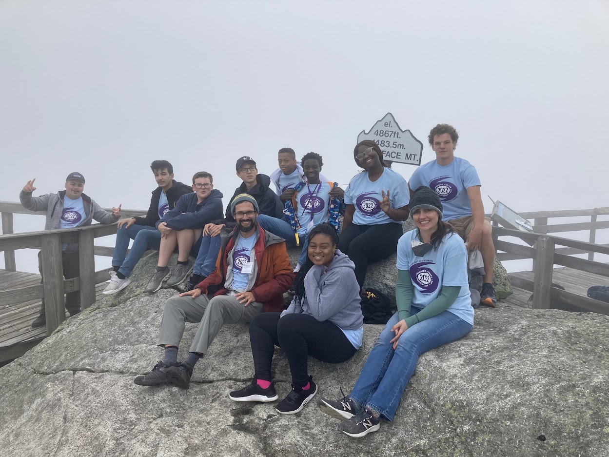 UAlbany weather camp students and faculty leaders sit on rocks atop the Whiteface Mountain summit..