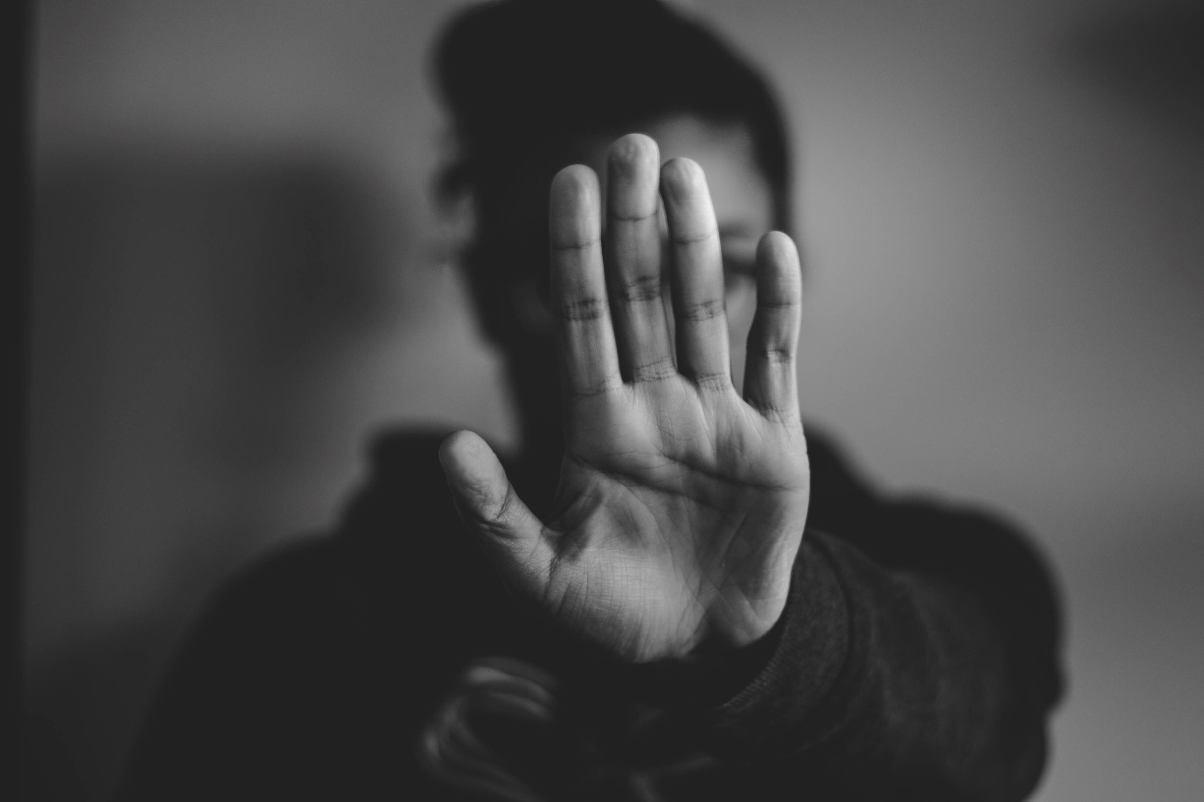 A person holds up their hand in front of their face with their palm outwards.