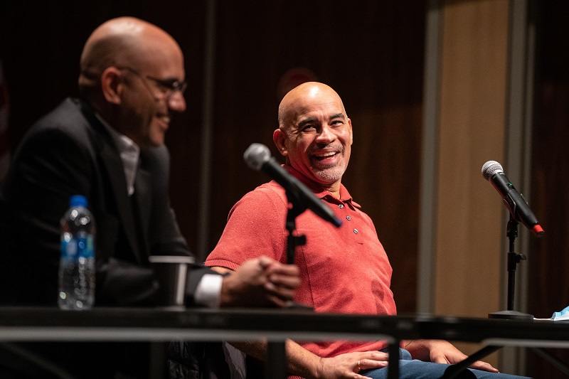 NYS author Ayad Akhtar and NYS poet Willie Perdomo sit side by side laughing at a table in front of two microphones during a panel discussion at UAlbany.