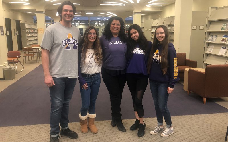 Four members of the UAlbany Student Stories podcast team pose smiling with Associate Professor Carmen Serrano (center) in the University Library.