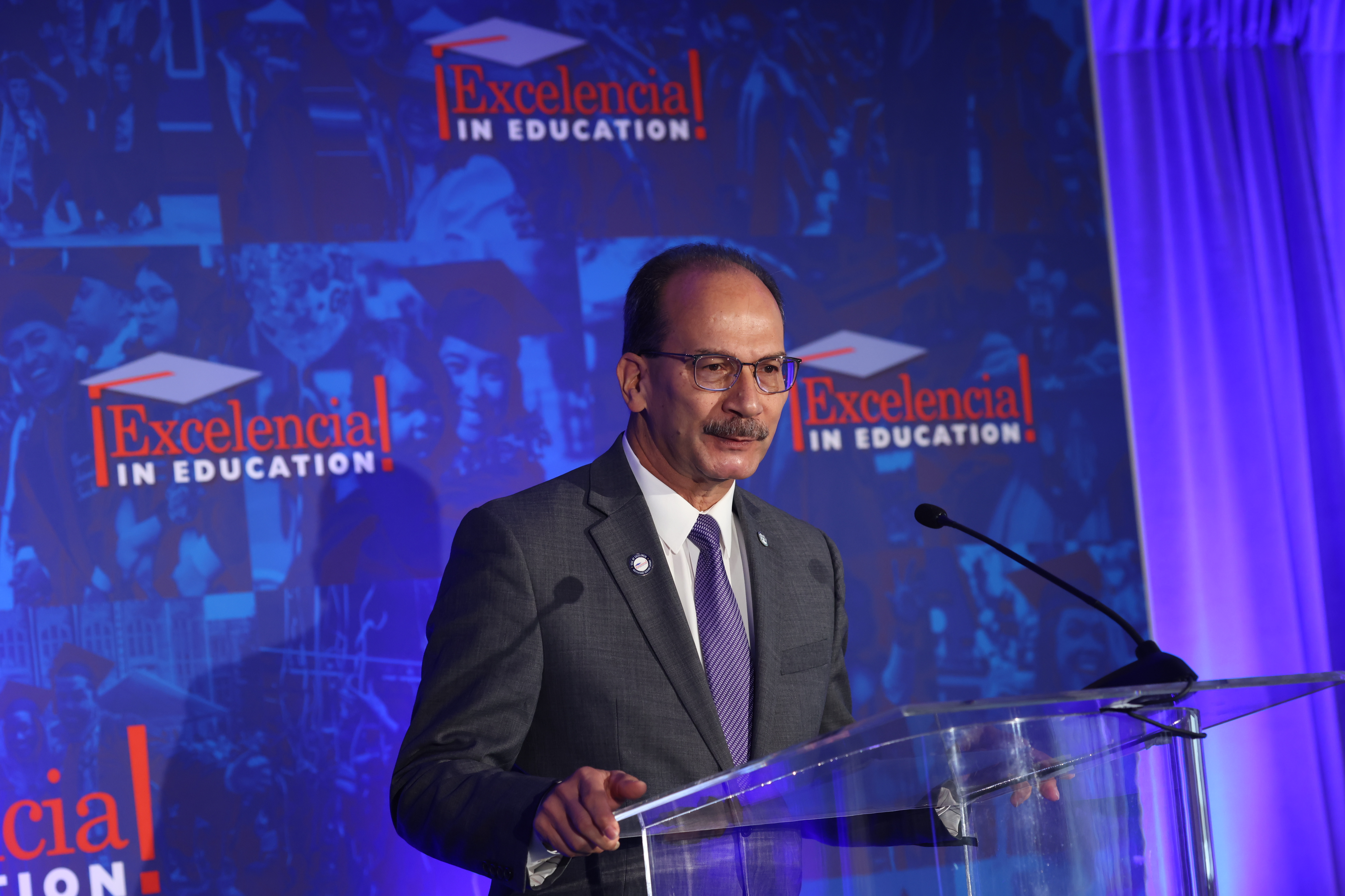 UAlbany President Havidán Rodríguez stands at a clear plastic podium in front of an Excelencia in Education banner to accept the Seal of Excelencia on behalf of UAlbany.