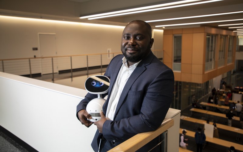 Benjamin Yankson, in a white shirt and blue suit jacket, holds a small robot with a face