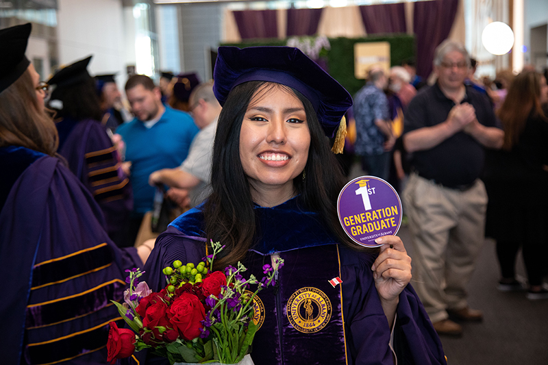 Doctoral student at commencement holding a '1st Generation Graduate' sticker.