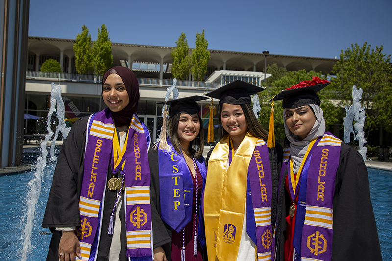 Four female students in regalia on campus.