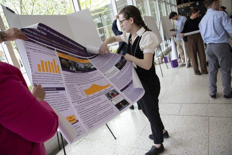 A woman in braids and glasses unrolls a research poster to place it on an display easle