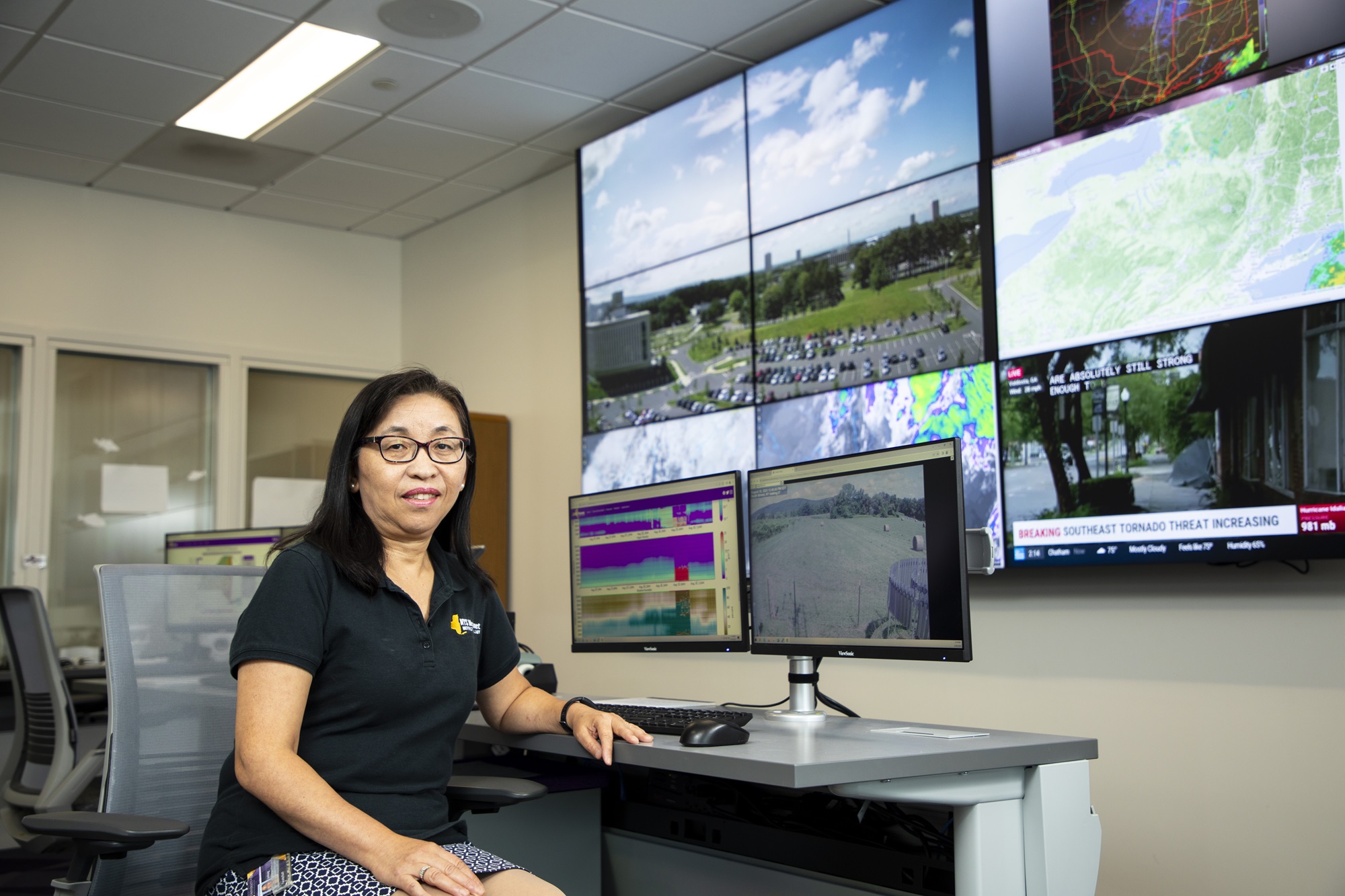 New York State Mesonet Director June Wang sits in front of screens in the network's operations center.