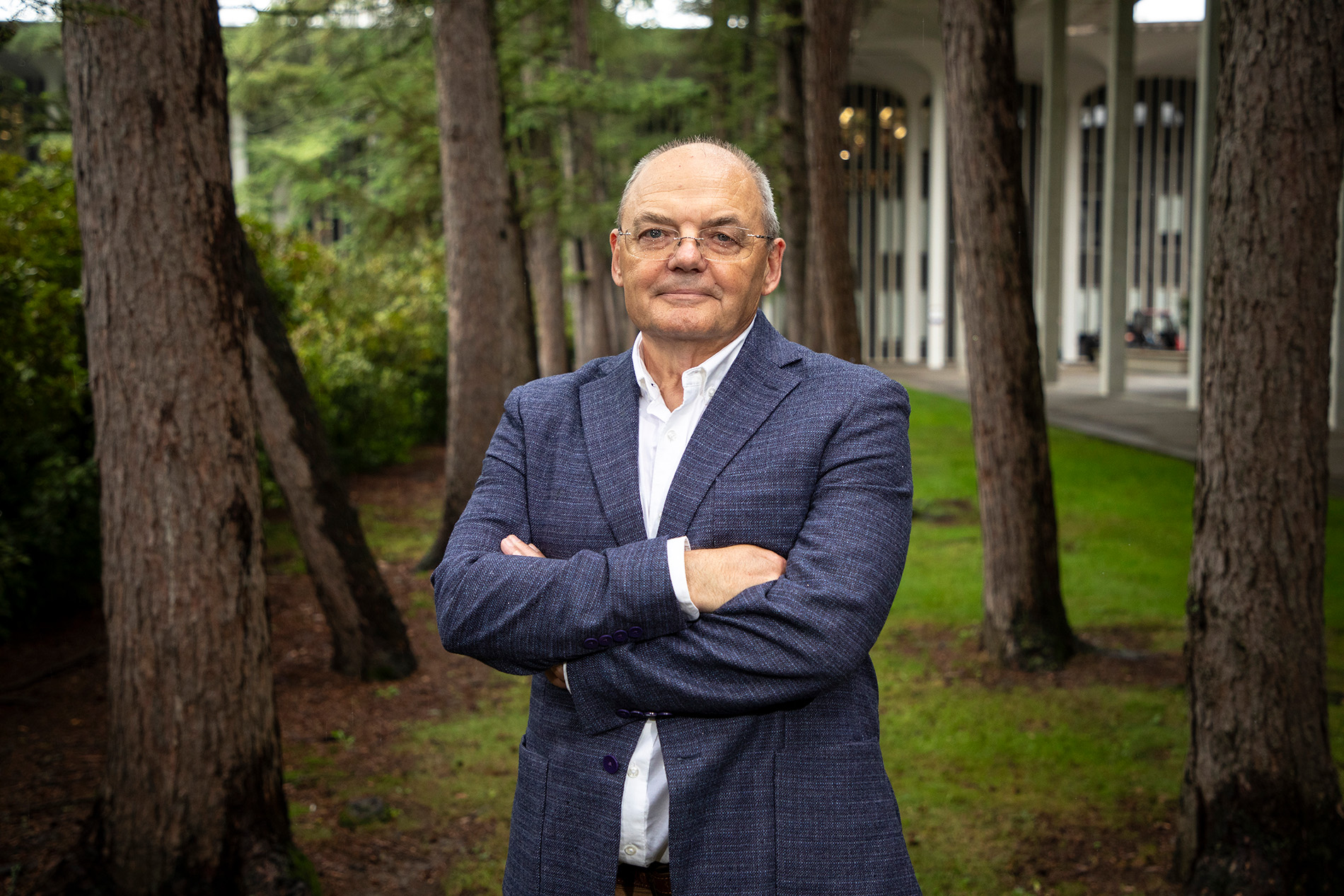 Andrei Lapenas stands in a suit with his arms folded in front of the Academic Podium courtyard on the Uptown Campus.