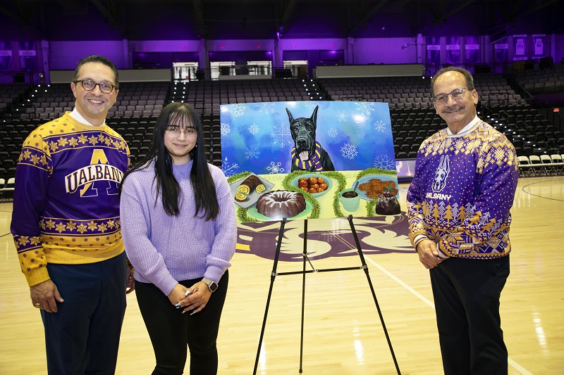 Three people standing smiling on a basketball court next to an easel with a digital drawing of a Great Dane drooling at a table full of holiday foods.