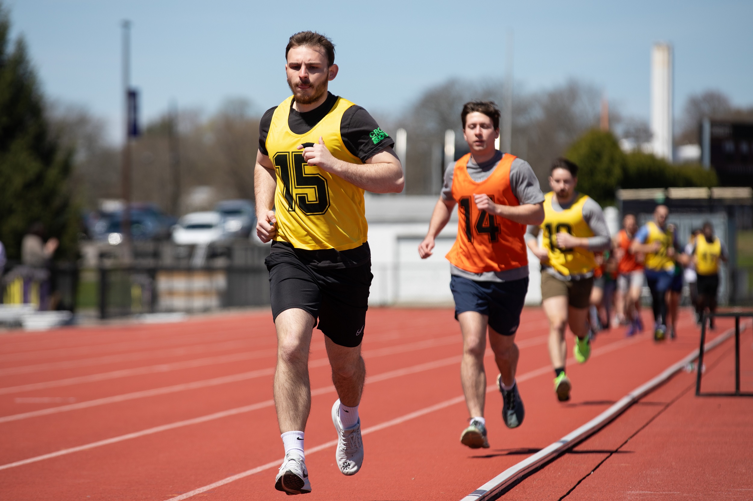 Students in yellow and orange jerseys run on the UAlbany track during the FBI physical fitness test.