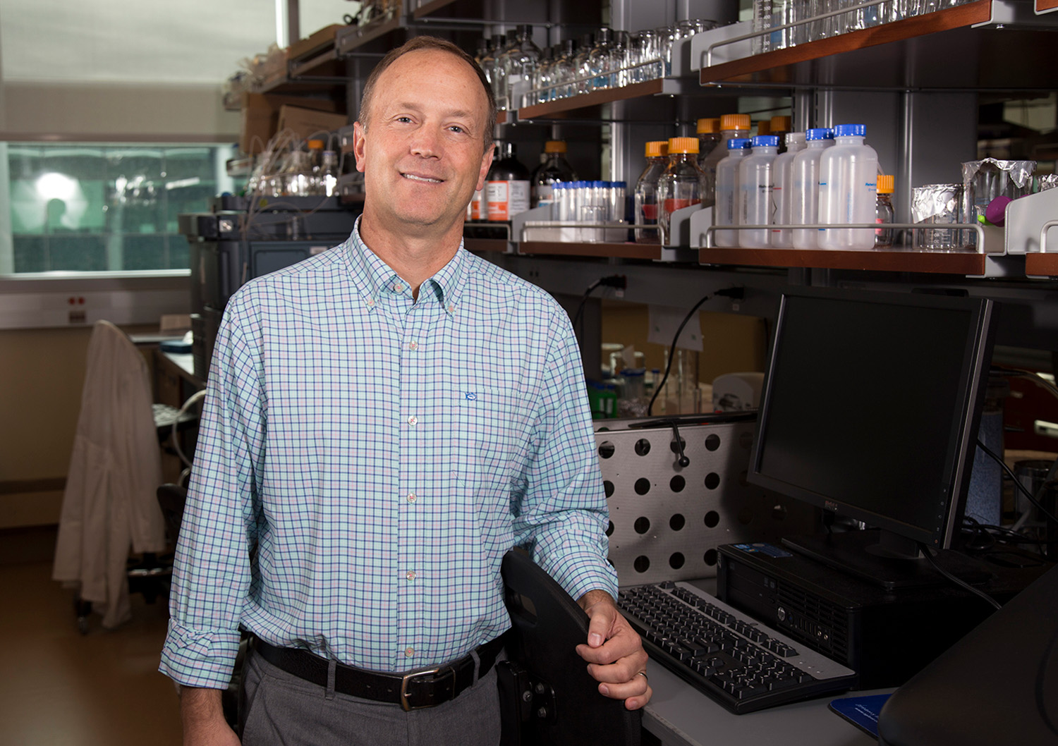 RNA Intstitute Director Andrew Berglund stands in his lab facing camera with a computer and many glass tubes in the background.