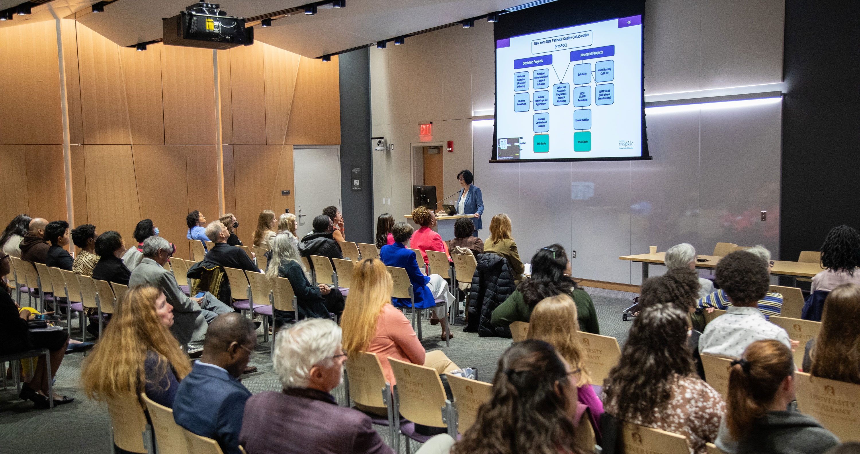 A researcher presents a slideshow in front of a seated audience.