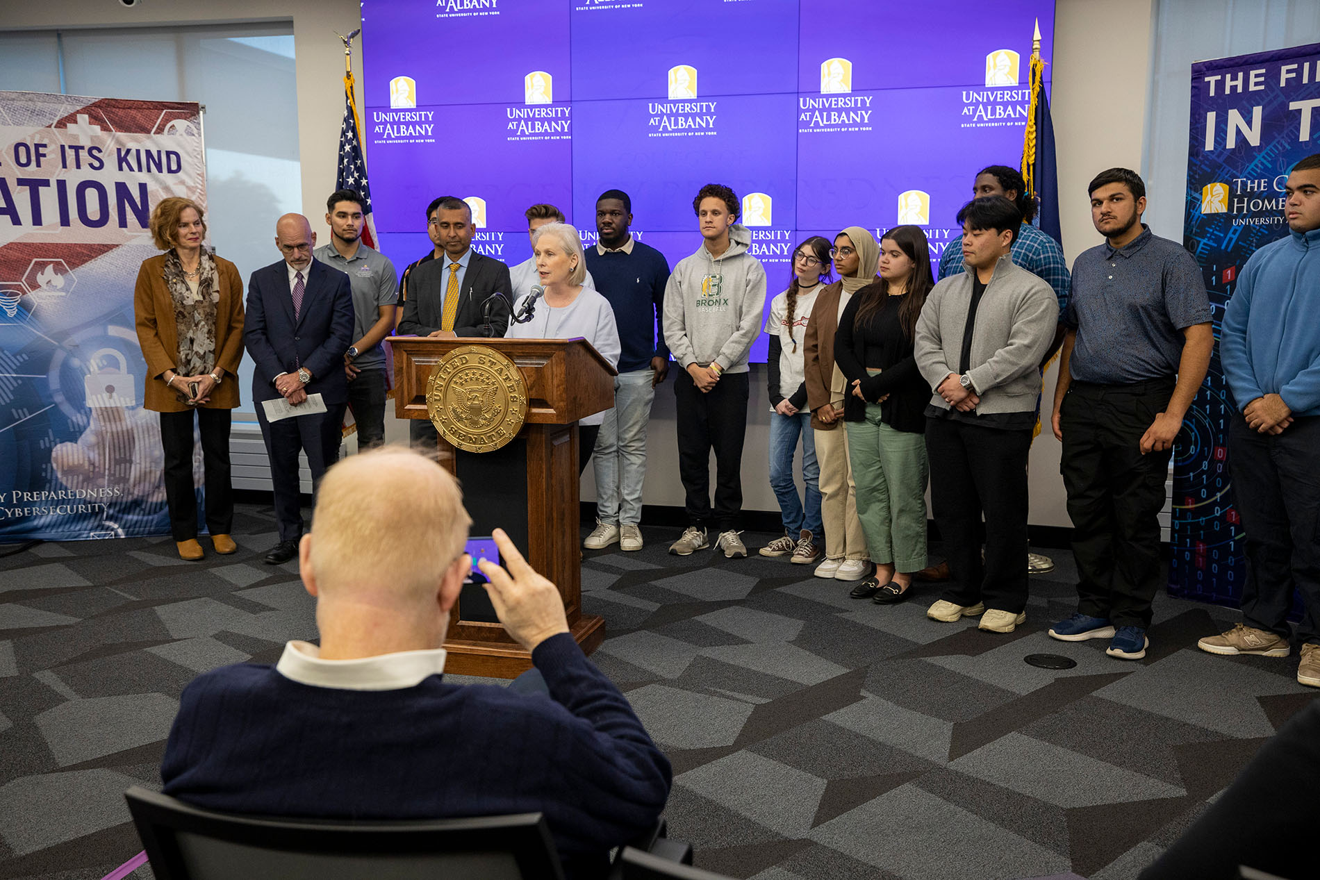U.S. Senator Kirsten Gillibrand stands with students behind the podium at the CEHC Ops Command Center.