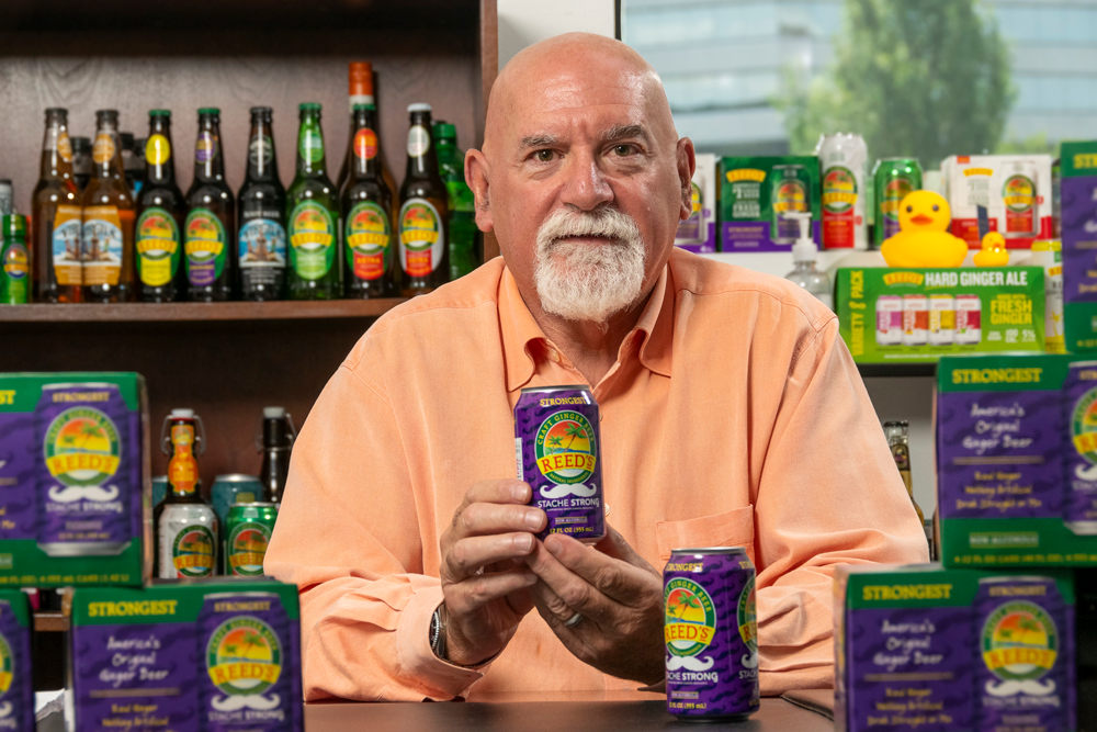 Norm Snyder sitting at a table filled with cans and bottles of Reed's soda. 