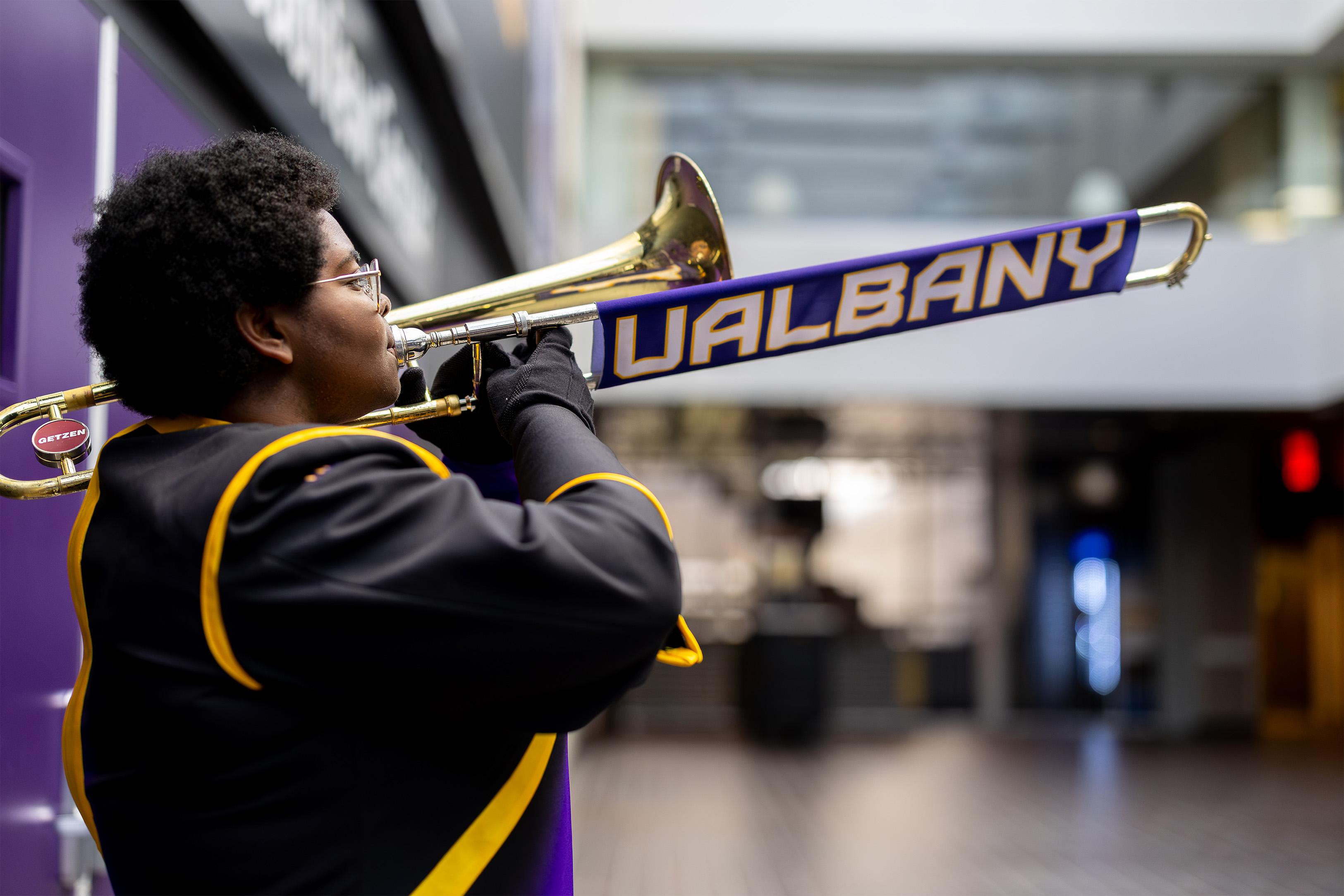 A student plays a trombone that has a slide cover that reads "UAlbany" in purple, white and gold.